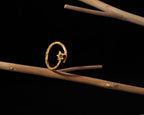A gold ring with a textured circular band and a small star-shaped centerpiece set with a green gemstone, displayed on a natural wooden branch against a solid black background.