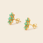 A pair of gold stud earrings featuring a cluster of small round-cut green gemstones, shown on a light beige background.