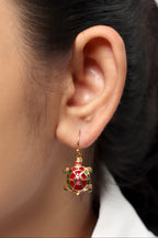 A close-up of a model's ear wearing a gold turtle-shaped drop earring with red, green, and white enamel details.
