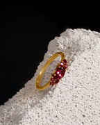 A gold ring with a cluster of faceted pink gemstones, displayed on a textured white stone against a solid black background.
