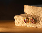A pair of gold-tone turtle drop earrings with red, green, and blue enamel detailing, displayed on a textured beige stone block against a dark background.