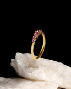 A gold ring with a row of small purple gemstones, displayed upright on a white crystalline rock against a solid black background.