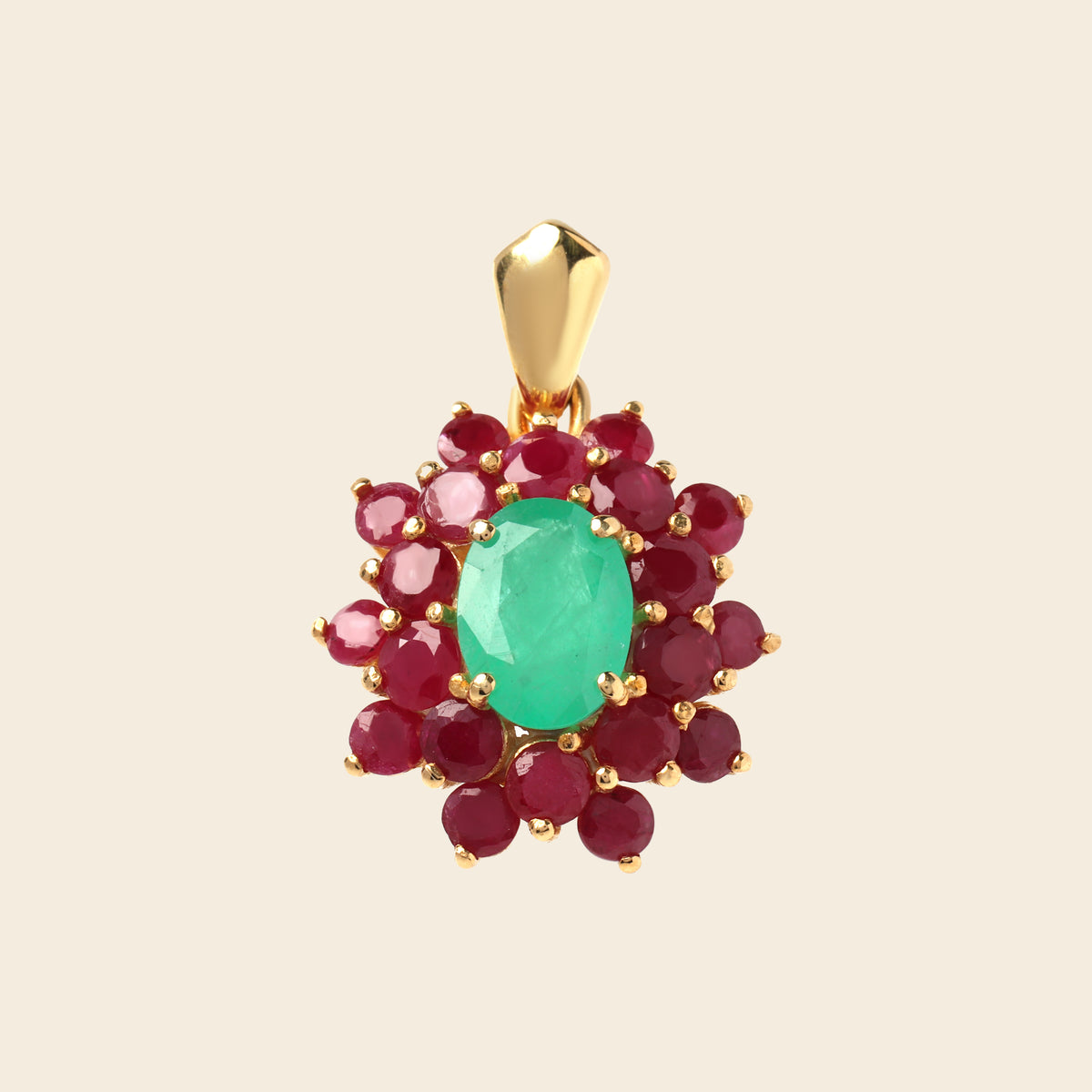 A gold pendant featuring a central oval-cut green emerald gemstone surrounded by a halo of round deep red ruby gemstones, set in a gold frame against a light beige background.