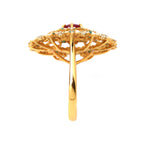 Gold ring with red gemstone, green accents, and diamond-like stones in floral filigree design