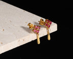 A pair of gold drop earrings with small pink gemstone clusters and teardrop-shaped gold drops, displayed on a white stone block against a black background.