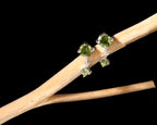 A pair of silver stud earrings with green gemstones, displayed on a light wood branch against a solid black background.