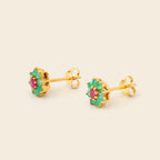 A pair of gold stud earrings with green enamel petals and a central pink gemstone, displayed on a light beige background.