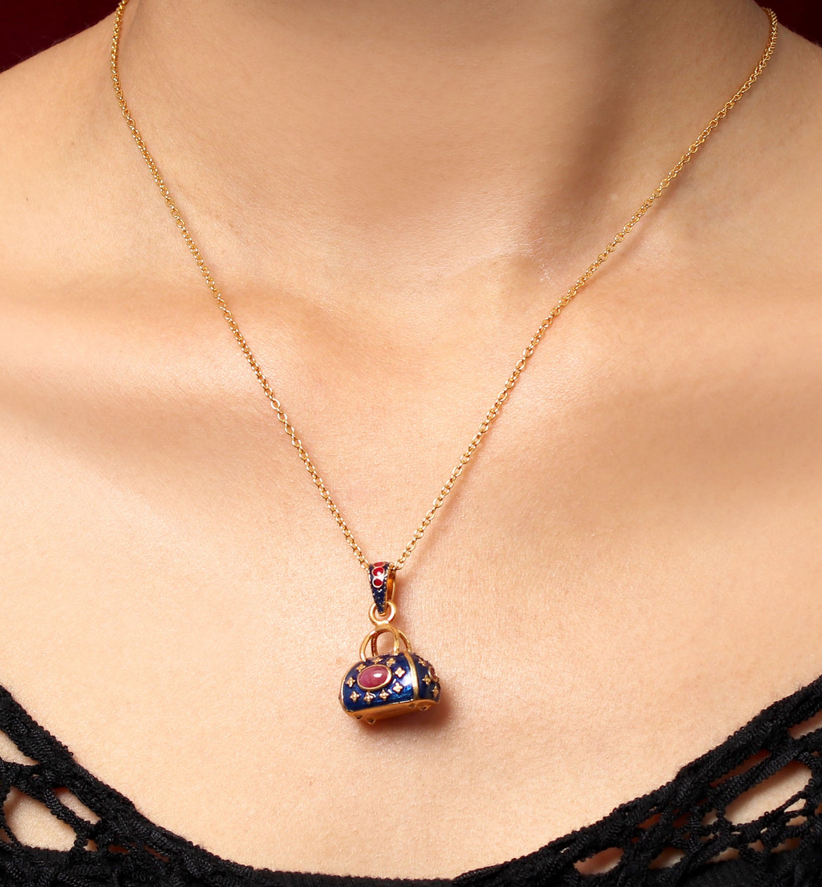 A gold chain necklace with a small handbag-shaped pendant featuring red and blue enamel detailing, shown worn on a model's neck.