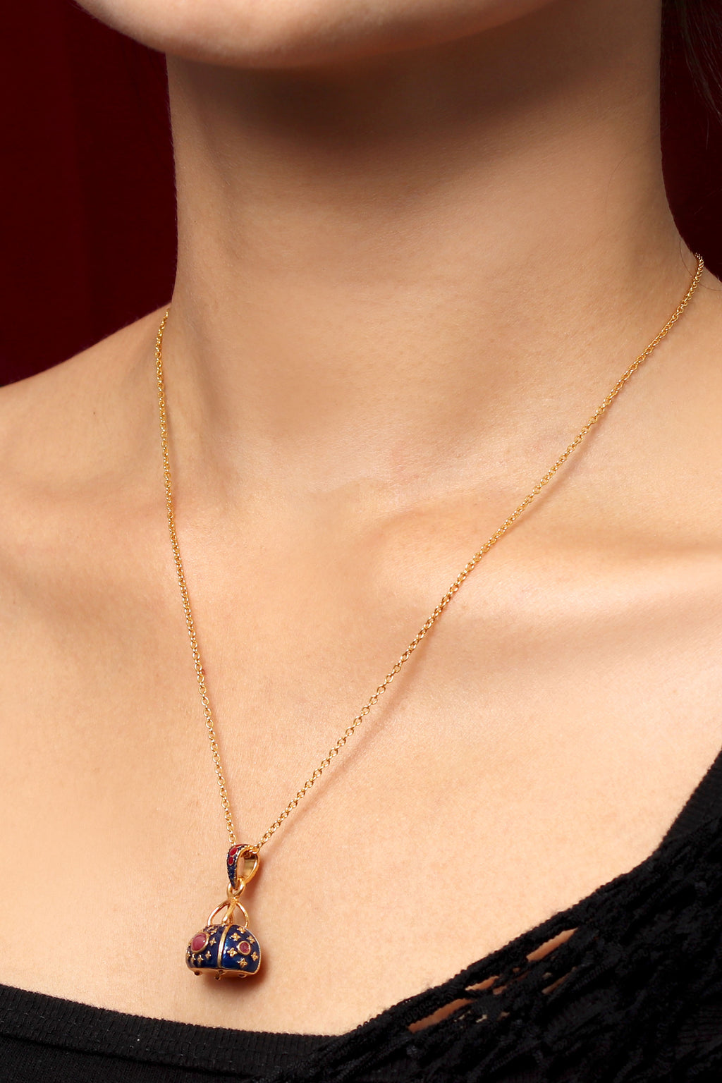 A close-up of a model wearing a delicate gold chain necklace with a small clover-shaped pendant featuring dark blue and gold enamel detailing.