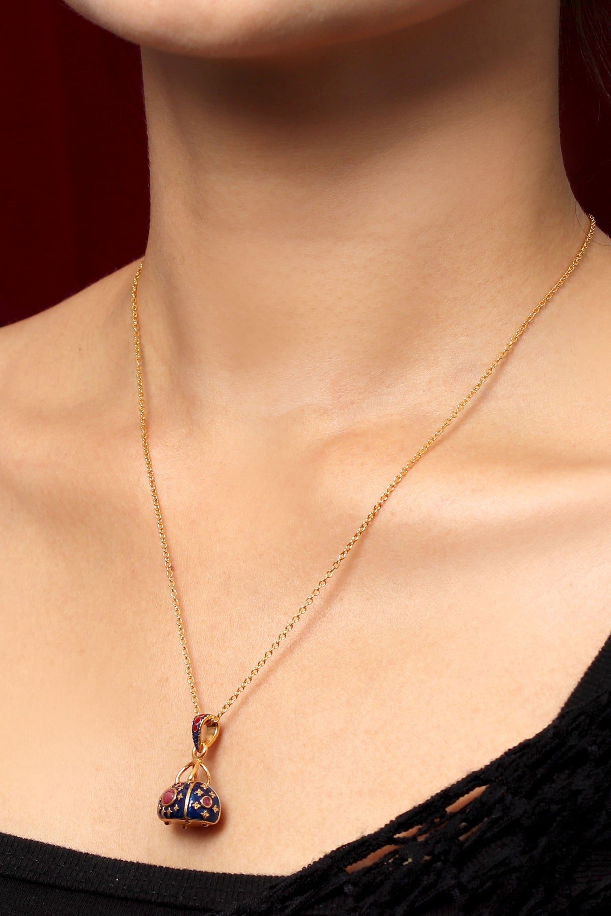 A close-up of a model wearing a delicate gold chain necklace with a small clover-shaped pendant featuring dark blue and gold enamel detailing.