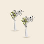 A pair of silver drop earrings featuring a cluster of four light green gemstones in a square setting, with a teardrop-shaped white stone dangling below, shown on a light beige background.