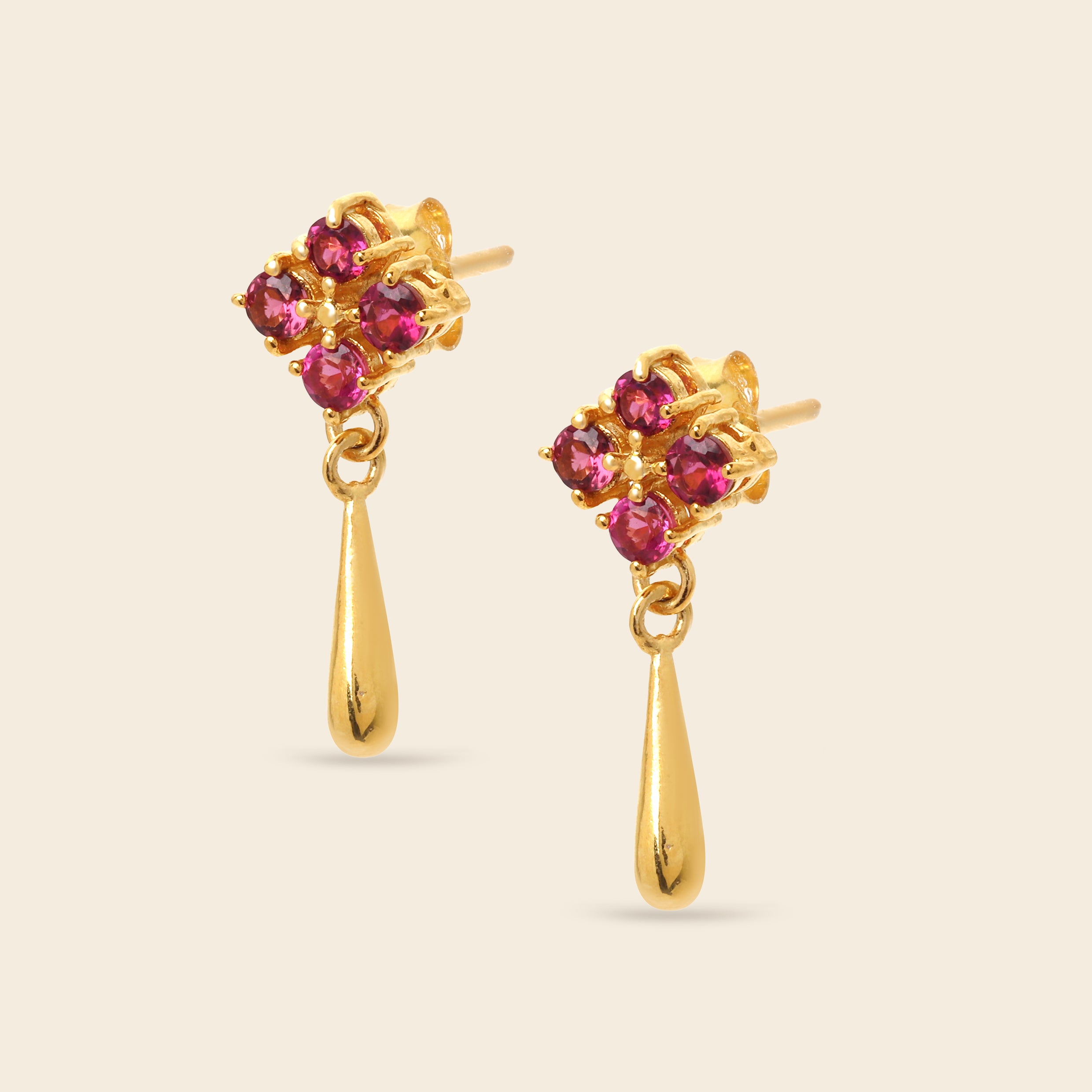 A pair of gold dangle earrings with a cluster of round pink gemstones at the top and a teardrop-shaped gold drop below, shown on a light beige background.