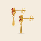 A pair of gold drop earrings with small rectangular pink gemstone accents and teardrop-shaped gold dangles, shown on a light beige background.