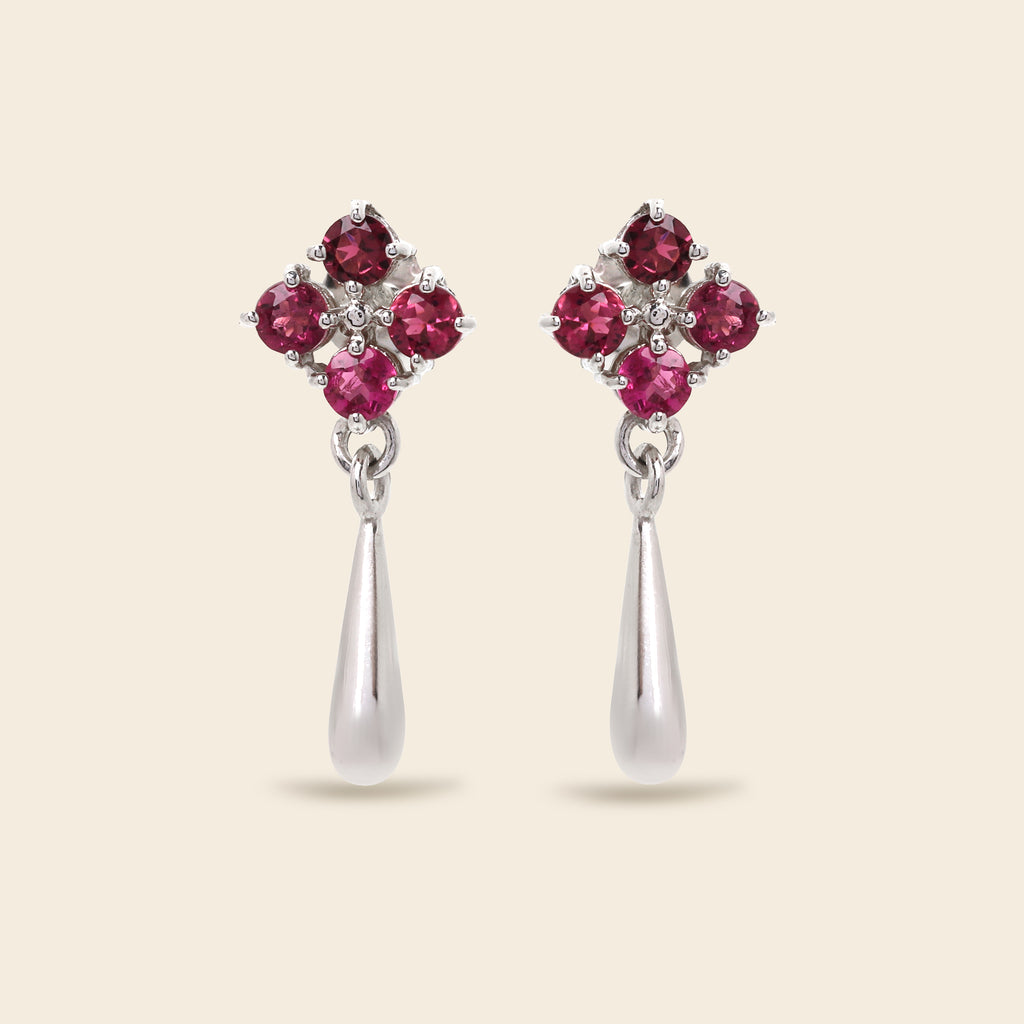 A pair of silver dangle earrings featuring a four-stone floral cluster at the top with four round pinkish-red gemstones and a teardrop-shaped silver drop below, set against a solid light beige background.