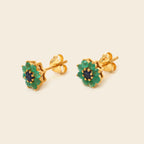 A pair of gold flower-shaped stud earrings with green outer petals and a dark blue center, shown on a light beige background.