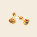 A pair of gold stud earrings with a geometric cage setting holding small multicolored gemstones, shown on a plain beige background.