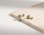 A pair of silver stud earrings with green gemstones, displayed on a light beige stone slab against a clean white background.
