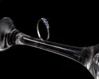 A silver ring with a row of small clear stones, displayed on the stem of a clear glass goblet against a solid black background.
