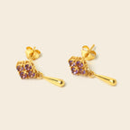 A pair of gold dangle earrings with a cluster of small purple gemstones and a teardrop-shaped drop, shown on a light beige background.