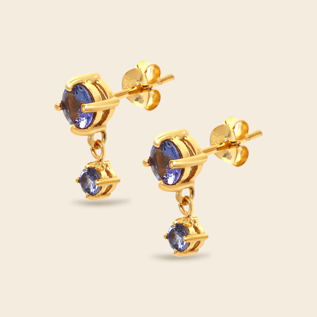 A pair of gold drop earrings featuring round blue gemstones, shown on a light beige background.