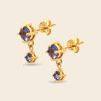 A pair of gold drop earrings featuring round blue gemstones, shown on a light beige background.