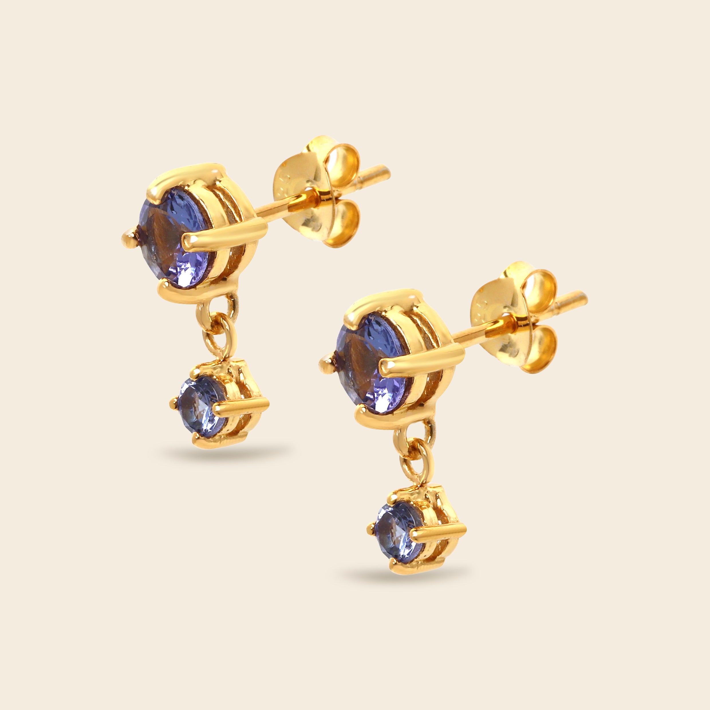 A pair of gold drop earrings featuring round blue gemstones, shown on a light beige background.