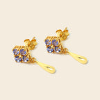 A pair of gold drop earrings featuring a cluster of round-cut light blue gemstones at the top and a polished gold teardrop drop below, set against a solid light beige background.