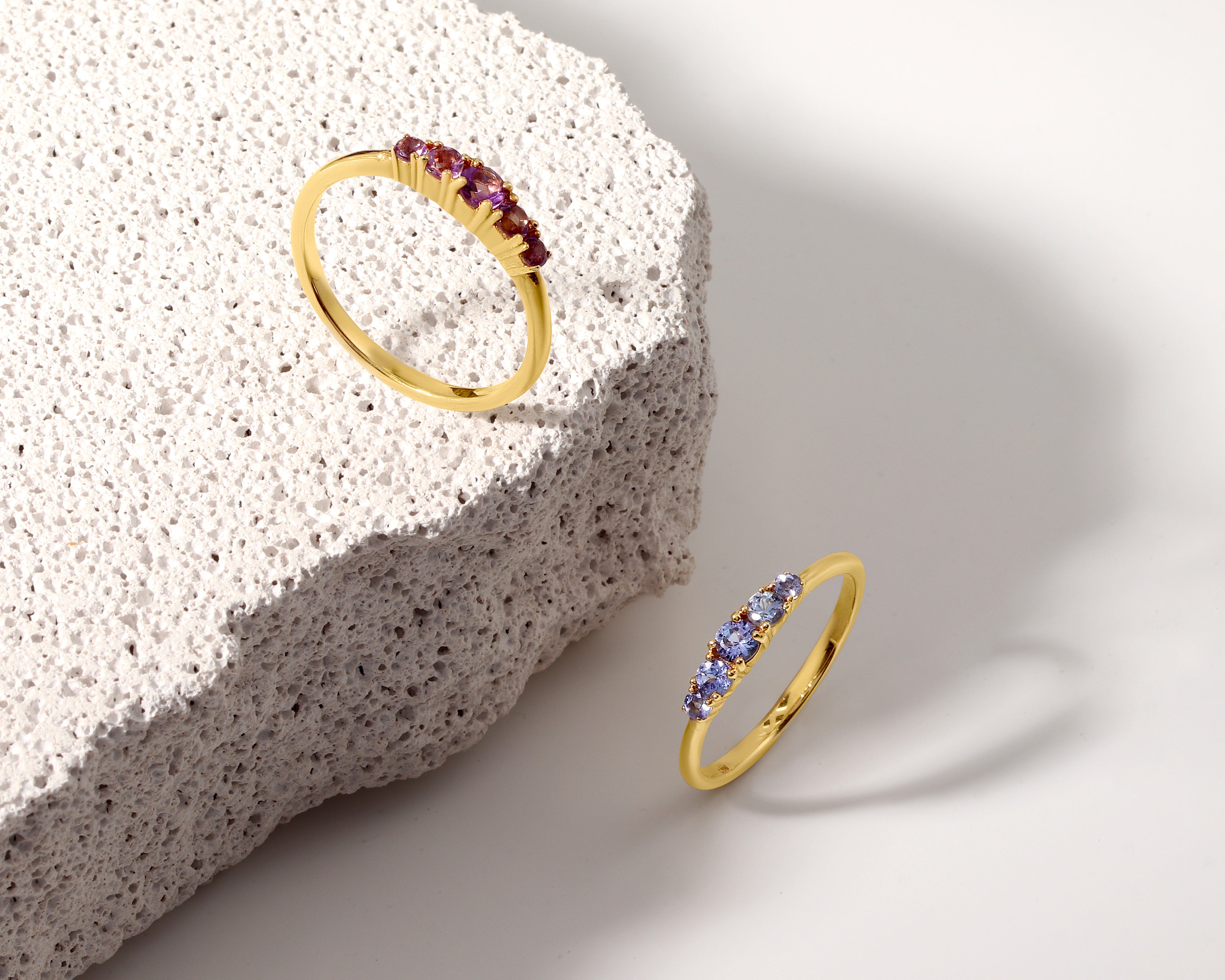 Two gold rings displayed on a white surface next to a textured stone slab.