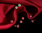 A set of colorful flower-shaped stud earrings arranged on draped dark red satin fabric against a black background.