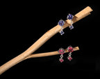 A pair of silver-tone drop earrings with blue gemstones on one branch and a pair with pink gemstones on the other, displayed against a solid black background.