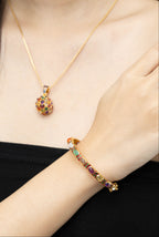 A close-up of a model wearing a gold necklace with a colorful gemstone pendant and a matching gold bracelet with multicolored stones.