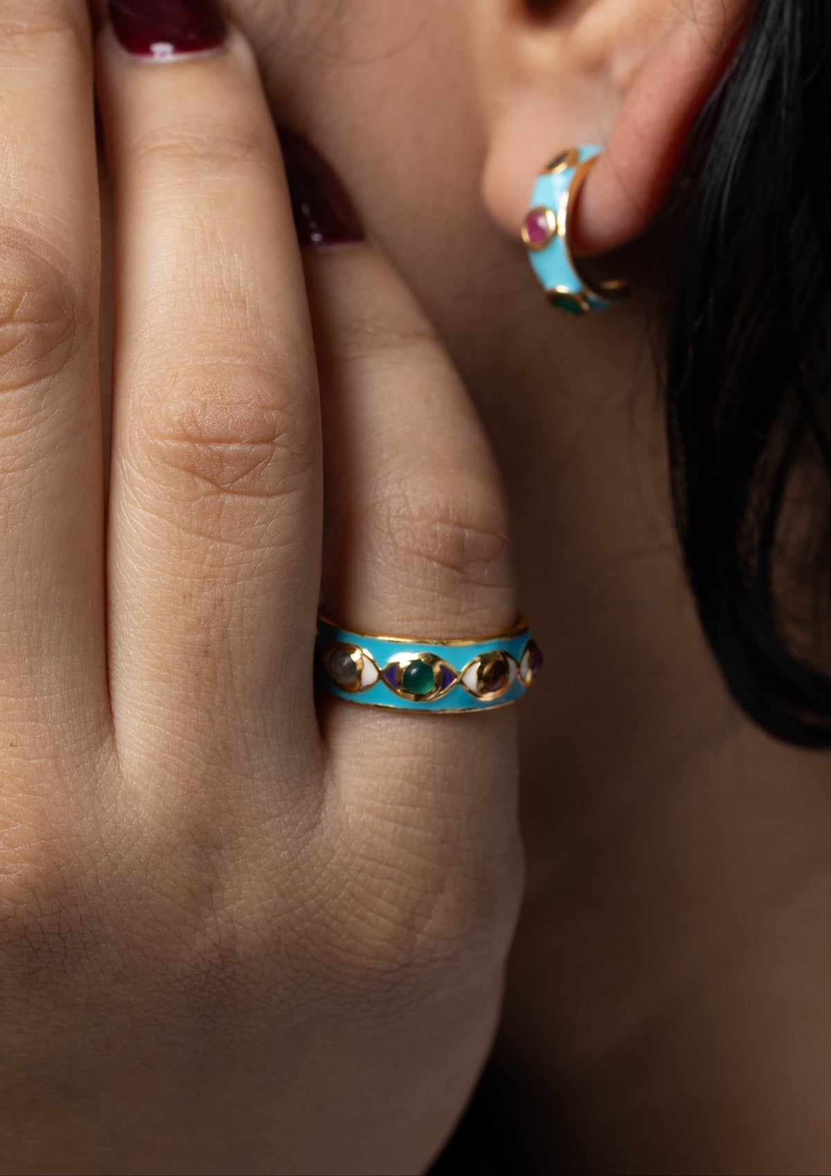 Close-up of a person wearing a turquoise and gold crescent moon hoop earring and a matching ring with small red and white accents.