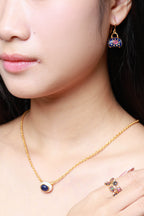 Close-up of a woman wearing a gold necklace with a round evil eye pendant, a matching gold hoop earring, and a gold ring with colorful gemstones.