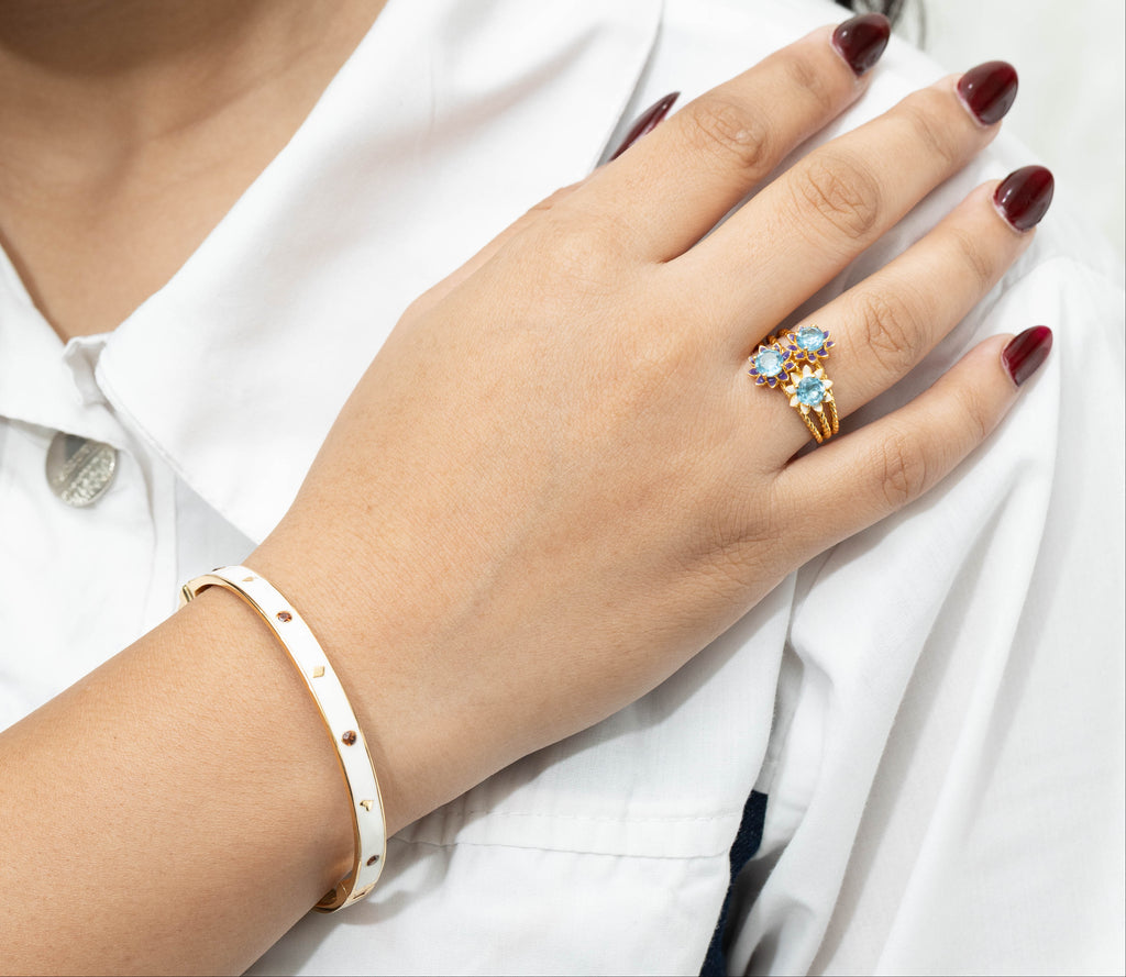 Close-up of a person wearing a ring with a colorful gemstone, earring, and bracelet on a white background.