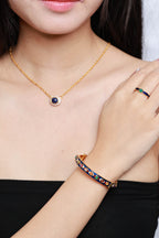 A gold ring with blue and green stones is also visible on the model's hand.