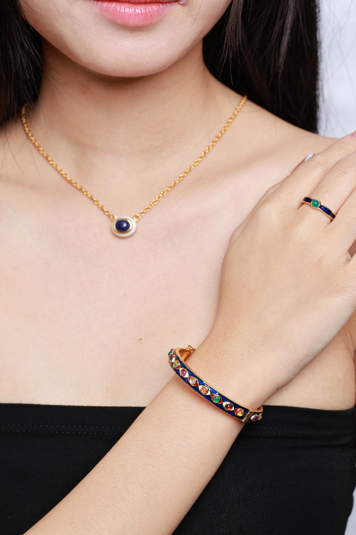 A gold ring with blue and green stones is also visible on the model's hand.