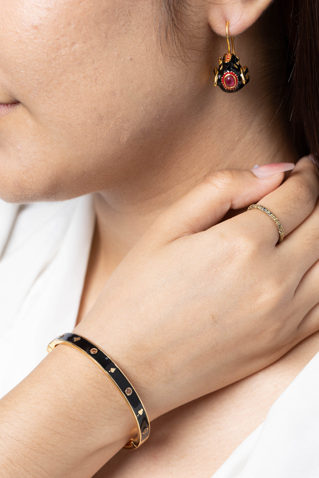 Close-up of a woman wearing a black and gold bangle bracelet, a matching ring, and a dangling earring with a red gemstone.