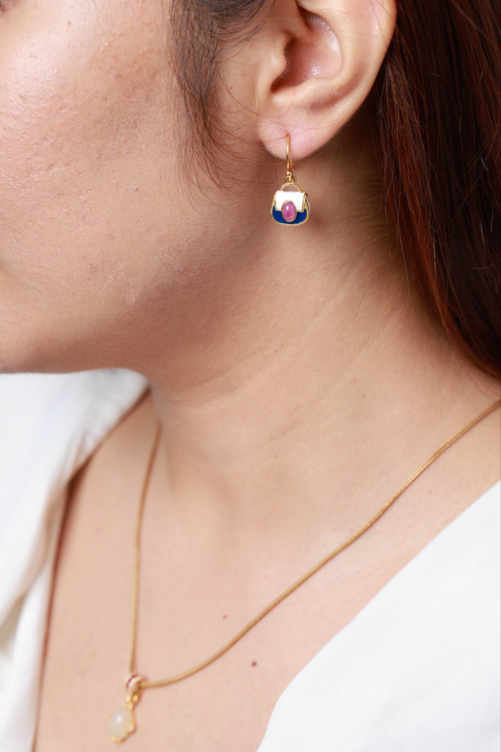 A close-up lifestyle shot of a woman wearing a delicate gold dangle earring with a colorful enamel face and a matching gold necklace.