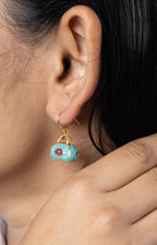 A close-up lifestyle shot of a model wearing a small turquoise and gold dangle earring and a matching turquoise and gold ring.