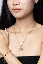 A woman wearing a delicate gold chain necklace with a floral pendant featuring green and pink stones, paired with a matching gold bracelet.