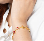 A close-up lifestyle shot of a woman wearing a matching gold-toned flower stud earring and bracelet, with her hand resting on her neck.