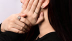 Close-up of a person wearing multiple rings and a small stud earring, with one hand covering part of the face.
