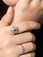 Close-up of a woman wearing delicate gold rings and a matching drop earring, with her hand resting against her cheek. 