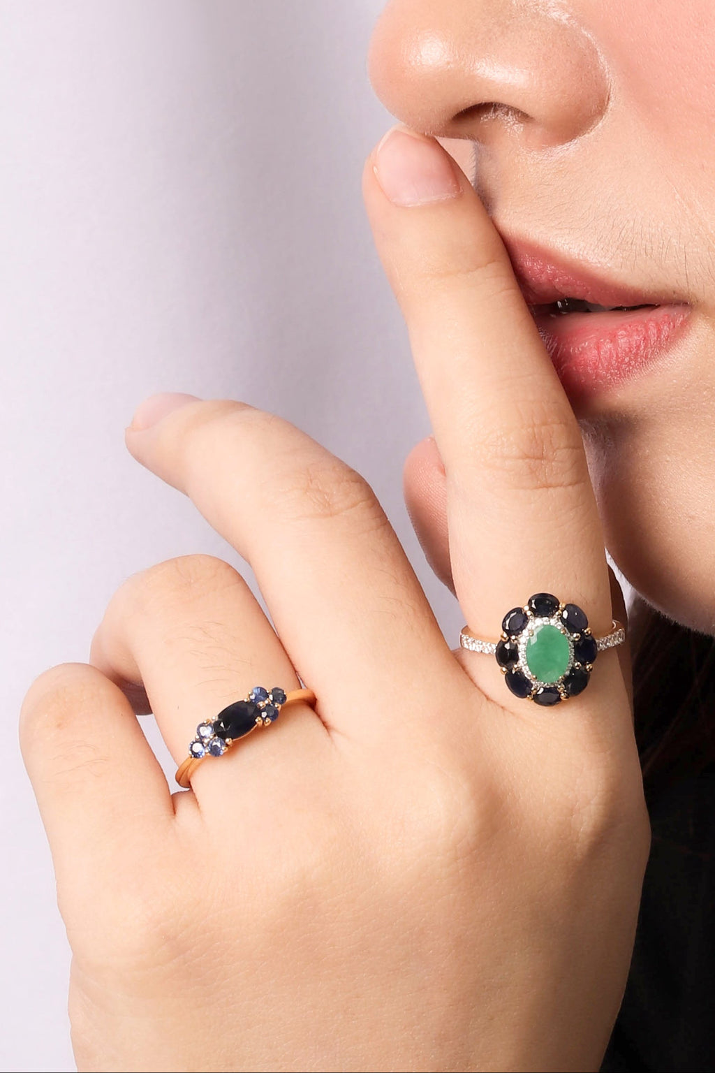 A close-up lifestyle shot of a person's hand and lower face wearing two silver rings. 