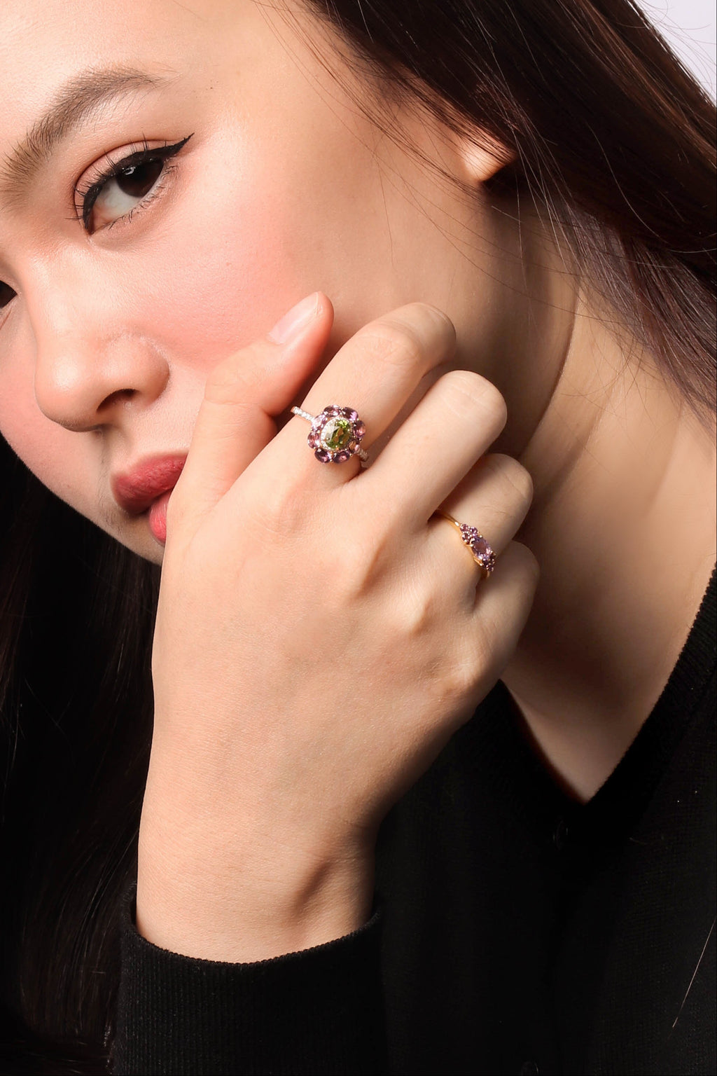 A close-up portrait of a woman wearing two rings on her fingers, with one ring prominently displayed on her index finger. 