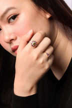 A close-up portrait of a woman wearing two rings on her fingers, with one ring prominently displayed on her index finger. 