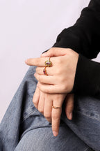 A close-up of a person's hands resting on their lap, wearing three gold rings with colorful gemstones .