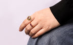 A close-up of a person's hand resting on their lap, wearing gold rings
