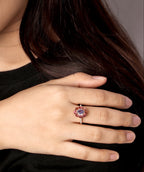 A close-up lifestyle shot of a woman wearing a rose gold ring with a round purple gemstone and a small gold crescent moon earring.