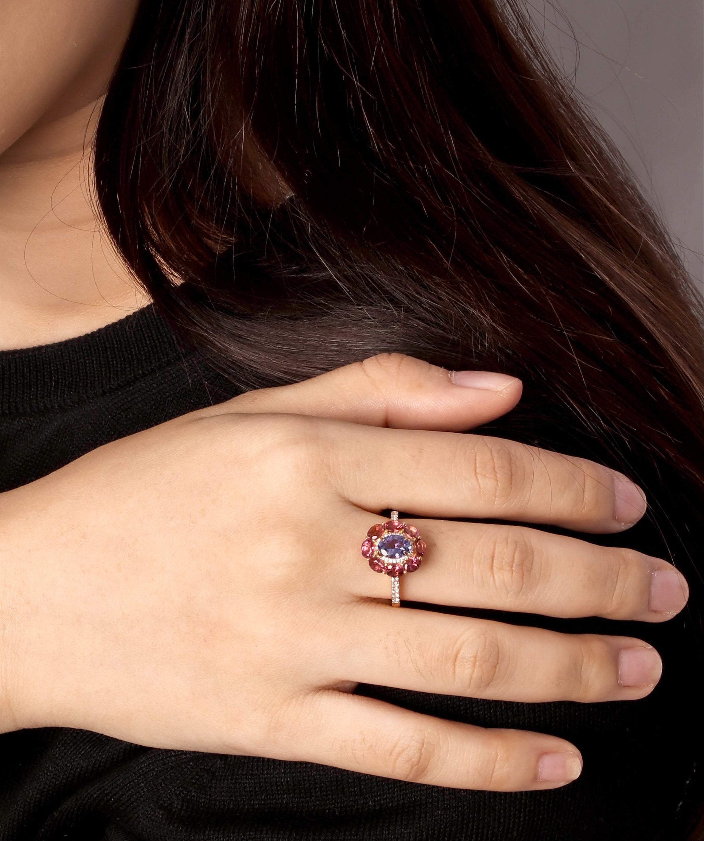 A close-up lifestyle shot of a woman wearing a rose gold ring with a round purple gemstone and a small gold crescent moon earring.